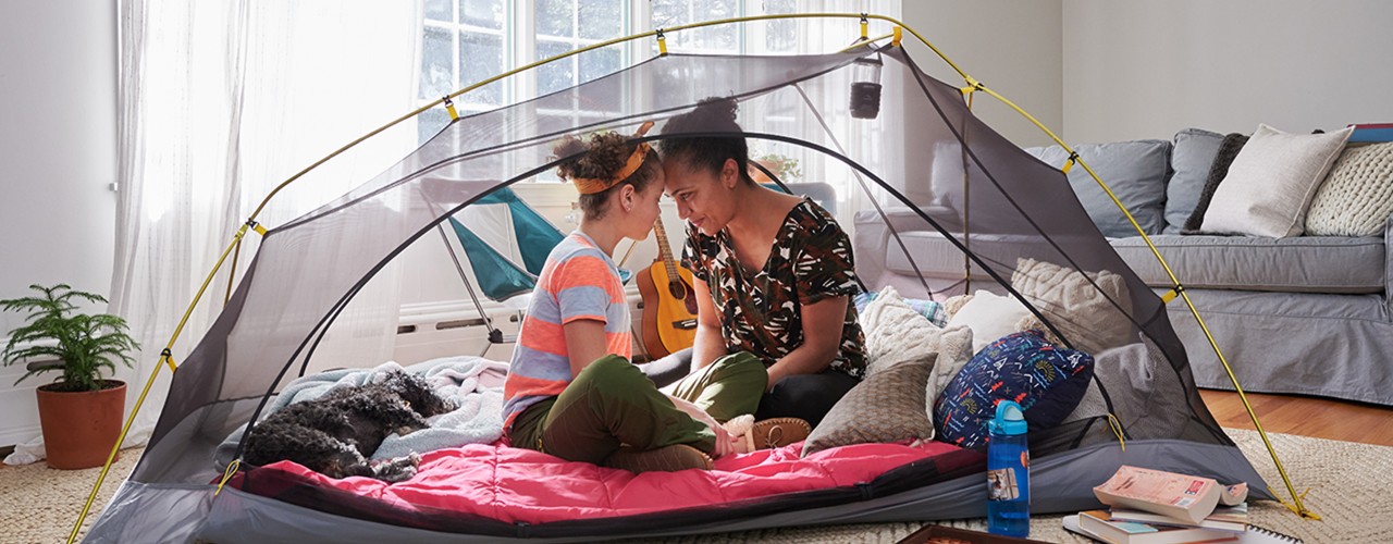 Mom and child sitting in a tent in their living room, indoor camping.